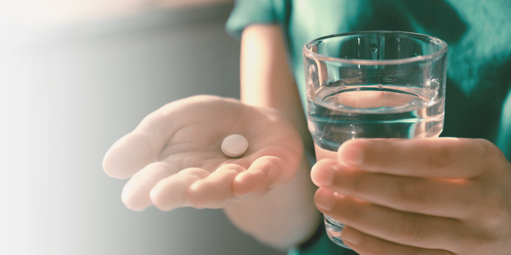 hands hold a glass of water and a round pill