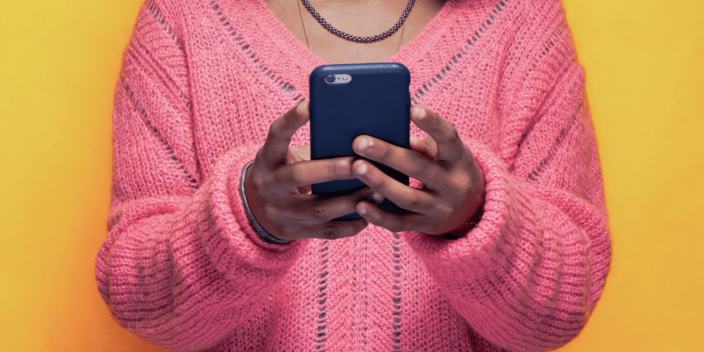 Young woman in pink sweater holds phone in navy phone case in both hands.