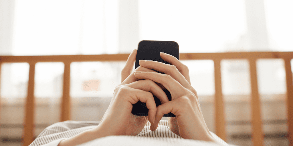 Person holds a phone while laying in bed