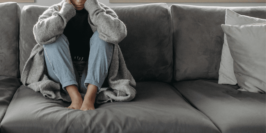 Woman in jeans, black tee, and gray sweater sets on a gray couch.