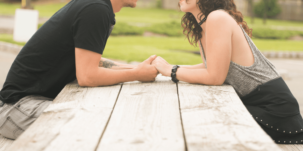 Couple setting across from each other at a picnic table, holding hands