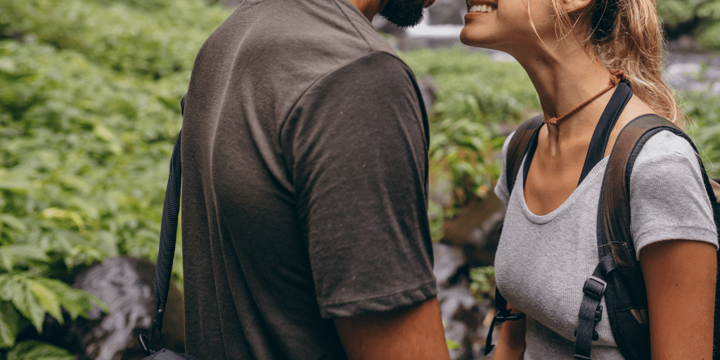 A couple smiles at one another while standing outside